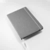 Libreta Ecológica Viena de cartón reciclado con 80 hojas rayadas y banda elástica para kits de bienvenida y eventos. Detalle en gris