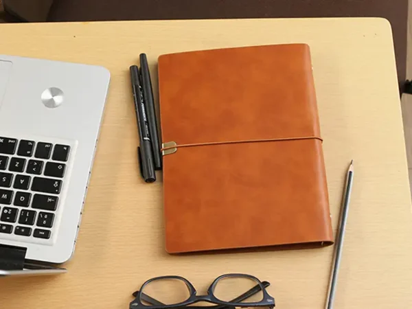 Libreta Corvino tipo carpeta en poliuretano con cierre de resorte y detalle metálico para laboratorios farmacéuticos. Muestra libreta sobre escritorio