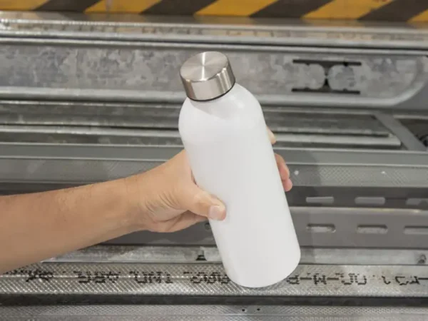 Botella de aluminio Tulum acabado mate colores negro blanco y azul con tapa de acero inoxidable para merchandising automotriz de Dot Factory. Muestra de cilindro en la mano de una persona