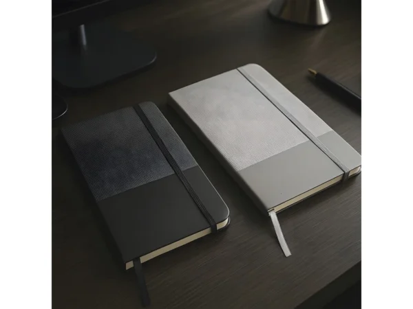 Libreta GAM con tapa bicolor de poliuretano suave al tacto, hojas crema rayadas y cierre de banda elástica.